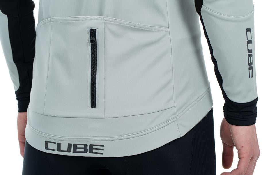 Eine Person trägt eine schwarz-graue, wind- und wasserabweisende CUBE TEAMLINE Multifunktionsjacke mit einer Rückentasche mit Reißverschluss; das CUBE-Logo befindet sich auf dem unteren Rücken und dem rechten Ärmel. Nur der Oberkörper und die Arme sind sichtbar.