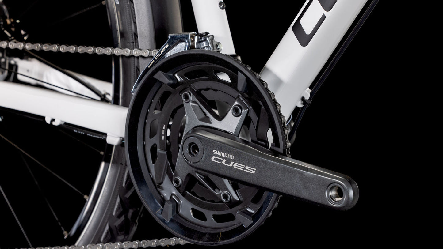 Nahaufnahme einer Shimano CUES-Kurbelgarnitur und Kette mit dem Logo auf dem Kurbelarm, montiert auf einem CUBE Nature Pro Allroad cotton'n'grey 2025 Aluminiumrahmen mit schwarzem Hintergrund.