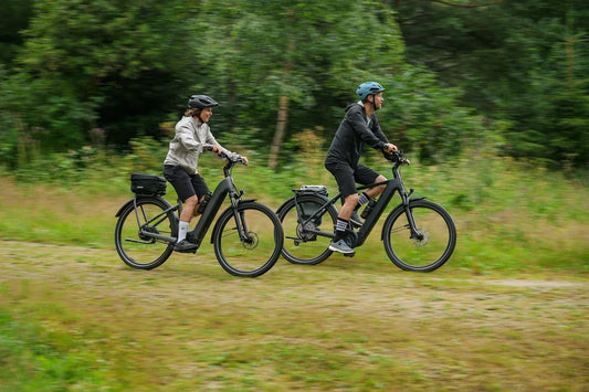 Zwei Personen fahren nebeneinander auf CUBE Trekking-E-Bikes durch eine grüne Naturlandschaft