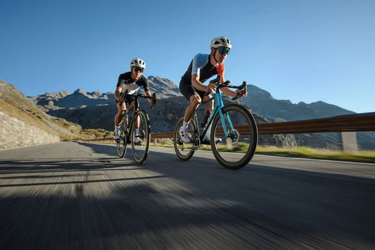 Zwei Rennradfahrer auf CUBE Rennrädern auf einer Passstraße vor schneebedeckten Bergen