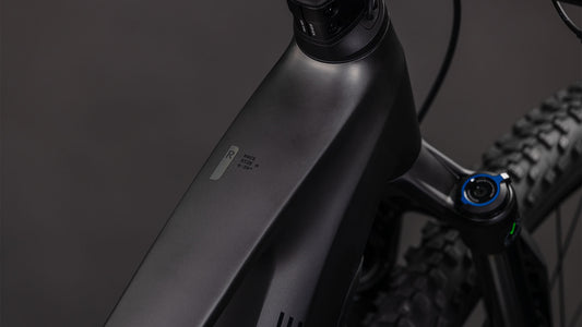 Nahaufnahme des mattschwarzen CUBE Stereo Hybrid ONE22 Race 800 slabgrey'n'chrome 2026 Rahmens, der das Oberrohr, die Vorderradaufhängung, die Shimano 12-fach XT Schaltung und das Reifenprofil vor einem dunklen Hintergrund hervorhebt.