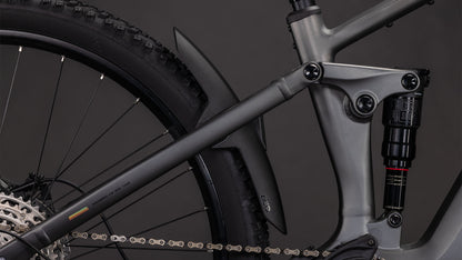 Nahaufnahme der Hinterradfederung und des Shimano XT-Antriebs des CUBE Stereo Hybrid ONE22 Race 800 slabgrey'n'chrome 2026 mit Hinterrad, Stoßdämpfer, Kette und mattschwarzem Schutzblech vor dunklem Hintergrund.
