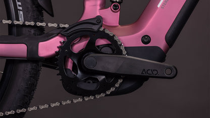 Nahaufnahme einer schwarzen Kurbelgarnitur mit dem Schriftzug "ACID" auf Arm und Kettenblatt, montiert am rosafarbenen CUBE Stereo Hybrid ONE22 Race 800 shiftblush'n'black 2026 Rahmen, mit der Kette, einem Teil des Hinterreifens und der Shimano XT 12-fach Kompatibilität.