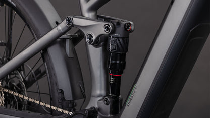 Nahaufnahme des CUBE Stereo Hybrid ONE22 Race 800 FE slabgrey'n'chrome 2026 Rahmens, die das mattgraue Finish, die Hinterradfederung mit RockShox Dämpfer und die sichtbare Kette in der Nähe des Hinterrads zeigt.