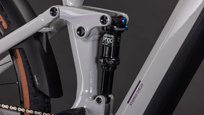 Nahaufnahme der Hinterradaufhängung und des Stoßdämpfers an einem CUBE Stereo Hybrid ONE22 SLX 800 greige'n'switch 2026, mit einem Teil des Hinterreifens - ideal für Fahrer, die die Vorteile von E-Fully und Bosch CX Antrieb nutzen möchten.