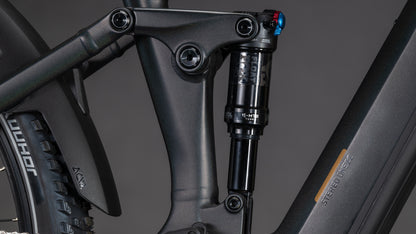 Nahaufnahme eines schwarzen CUBE Stereo Hybrid ONE22 SLT 800 prizmblack'n'black 2026 vollgefederten E-Mountainbike-Rahmens. Hervorzuheben sind der hintere Stoßdämpfer, das Gestänge, das sichtbare Reifenprofil und die Shimano XT Di2 Komponenten.