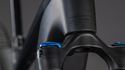 Nahaufnahme des CUBE Stereo Hybrid ONE22 SLT 800 prizmblack'n'black 2026 Rahmen und Gabel in mattem Schwarz, mit blauen Einstellknöpfen und einem dezent eingravierten Etikett, vor einem verschwommenen Hintergrund.