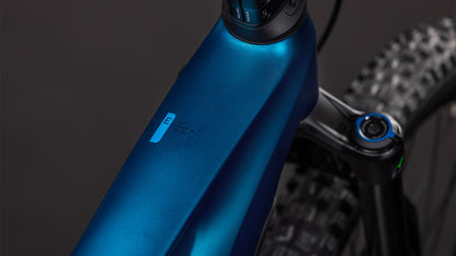 Nahaufnahme des Oberrohrs und der Vorderrad-Federgabel eines CUBE Stereo Hybrid ONE44 EX 800 electricblue'n'blue 2026, mit einem kleinen E-Etikett und einem Teil des strukturierten Reifens, vor einem dunklen Hintergrund.