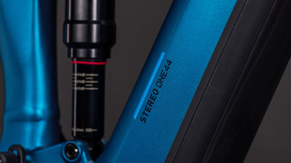 Nahaufnahme des CUBE Stereo Hybrid ONE44 EX 800 electricblue'n'blue 2026-Rahmens mit dem STEREO ONE44-Schriftzug, einem Teil des Aufhängungssystems, und mattschwarzen Akzenten vor dunklem Hintergrund.