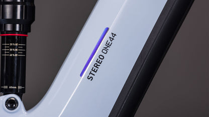 Nahaufnahme des CUBE Stereo Hybrid ONE44 EX 800 iceblue'n'prism 2026 Rahmens mit schwarzem STEREO ONE44 Aufdruck, einem lila Akzent, einem Teil der Federgabel mit Messmarkierungen und dem Bosch CX Antrieb auf der linken Seite.