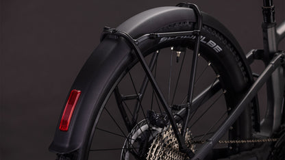 Nahaufnahme des Hinterrads des CUBE Stereo Hybrid ONE44 EXC 800 FE irongrey'n'chrome 2026, wobei ein schwarzes Schutzblech mit rotem Reflektor, eine Shimano XT-Kassette und ein Schwalbe-Reifen vor einem dunklen Hintergrund hervorgehoben werden.