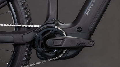 Nahaufnahme der CUBE Stereo Hybrid ONE44 HPC Race 800 blackline 2026 Kurbelgarnitur und Kette, mit schwarzen Pedalen, Kettenblatt, Carbonrahmen und dem nahtlos integrierten Bosch CX Motor. Einfarbig dunkelgrauer Hintergrund.