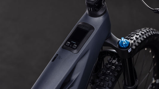 Nahaufnahme des CUBE Stereo Hybrid ONE44 HPC SLX 800 slabgrey'n'orange 2026 E-Mountainbike-Rahmens mit Digitalanzeige, Bedienelementen, Federgabel, Noppenreifen und integriertem Bosch CX-Motor vor dunklem Hintergrund.