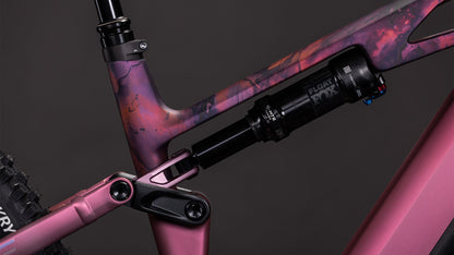 Nahaufnahme des CUBE Stereo Hybrid ONE44 HPC SLX 800 shiftblush'n'art 2026 Fahrradrahmens mit marmoriertem rosa und lila Finish, das die hintere Federung und den Stoßdämpfer vor einem dunklen Hintergrund hervorhebt.