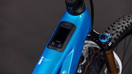 Nahaufnahme des blauen CUBE Stereo Hybrid ONE44 HPC AT 800 actionteam 2026 Rahmens mit integriertem Bosch Display am Oberrohr und leistungsstarkem Bosch CX Motor. Auch ein Teil der vorderen Federgabel und des Reifens ist zu sehen.
