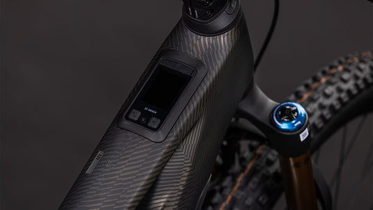 Nahaufnahme des CUBE Stereo Hybrid ONE44 HPC SLT 800 (carbongrid'n'chrome, 2026): zeigt das strukturierte Carbon-Oberrohr mit Digitalanzeige und Bedienelementen. Der Bosch CX-R-Motor, der 800-Wh-Akku, die Vorderradaufhängung und die Reifen unterstreichen seine All-Mountain-E-Bike-Power.
