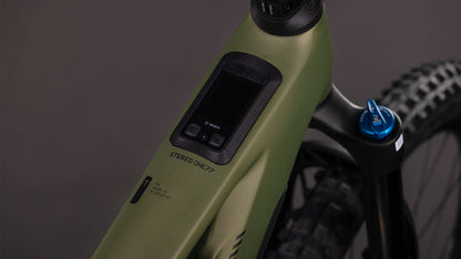 Nahaufnahme des Oberrohrs des CUBE Stereo Hybrid ONE77 HPC TM 800 (reedgreen'n'matrix, 2026) mit eingebauter Bosch CX-Motoranzeige und Bedienfeld. Der mattgrüne Rahmen mit der Aufschrift "STEREO ONE77", mit Hinterradreifen, blauer Gabel und 170 mm Federweg ist teilweise sichtbar.