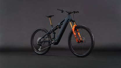Das CUBE Stereo Hybrid ONE77 HPC SLT 800 galaxy'n'orange 2026 E-Mountainbike mit markantem Rahmen und orangefarbenen Akzenten steht für Big-Mountain-Performance vor dramatischer Kulisse.