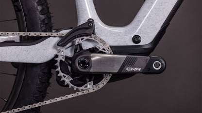 Nahaufnahme einer CUBE Cube AMS Hybrid ONE44 C:68X SUPER TM 400X Kurbelgarnitur und eines Pedalarms, die das Kettenblatt, die Kette und einen Teil des Carbonrahmens in foggrey'n'fibre 2026 vor einem dunklen Hintergrund zeigen.