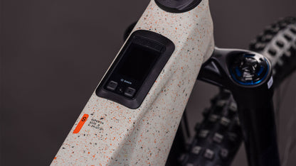 Nahaufnahme des CUBE AMS Hybrid 177 C:62 SUPER TM 600X (reedbeigegrit'n'orange, 2026) mit Bosch-Display, Bedientasten, Bosch CX-R-Motor, Fox Podium Federgabel, gesprenkeltem, grauweißem Rahmen, Warnaufkleber und Noppenreifen.