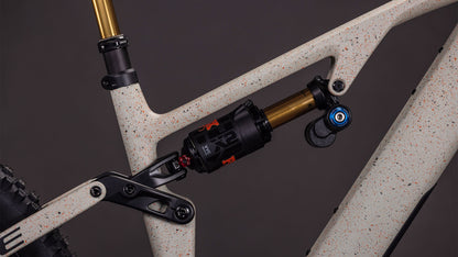 Nahaufnahme der CUBE AMS Hybrid 177 C:62 SUPER TM 600X Hinterradaufhängung, die einen schwarz-goldenen Stoßdämpfer auf einem gesprenkelten schilf-beigegrit'n'orangefarbenen Rahmen mit Hinterradreifen zeigt - ausgestattet mit einem Sram XX Eagle Getriebe.