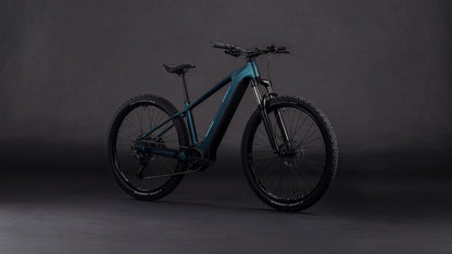 Das CUBE Reaction Hybrid ONE 800 royalgreen'n'prism 2026 mit dicken Reifen, einem schlanken Rahmen und einem leistungsstarken Bosch-Motor wird vor einem dunklen, neutralen Hintergrund präsentiert.
