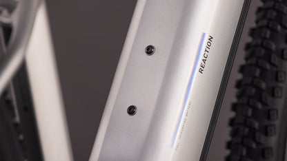Nahaufnahme des CUBE Reaction Hybrid ONE 800 sleekgrey'n'prism 2026 Rahmens mit zwei Befestigungsschrauben und "REACTION" Aufschrift. Ein knorriger Reifen ist sichtbar und deutet auf den Bosch-Motor und den leistungsstarken 800-Wh-Akku hin.
