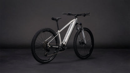 Das CUBE Reaction Hybrid ONE 800 sleekgrey'n'prism 2026 Mountainbike mit dicken Stollenreifen, mattsilbernem Rahmen und Bosch-Motor ist auf einem dunkelgrauen Hintergrund mit Front- und Seitenansicht abgebildet.