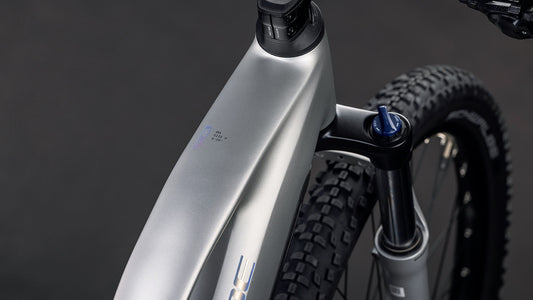 Nahaufnahme des CUBE Reaction Hybrid ONE 800 sleekgrey'n'prism Trapeze 2026 Rahmens, die das Oberrohr, den Bosch Motor, die Federgabel und den Vorderreifen vor einem dunklen Hintergrund zeigt.