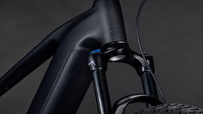 Die Nahaufnahme des CUBE Reaction Hybrid Pro 800 blackline 2026 E-Mountainbike-Rahmens zeigt die mattschwarze Federgabel, das Steuerrohr, das Vorderradsegment, die sichtbaren Kabel und den Bosch CX-Antrieb vor einem dunklen Hintergrund.