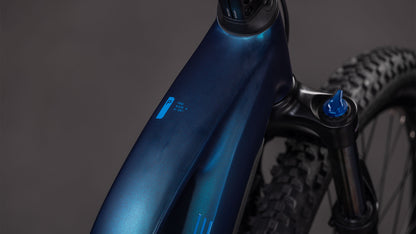 Nahaufnahme des CUBE Reaction Hybrid Pro 800 nebular'n'dazzle Trapeze 2026 Rahmens und der vorderen Federgabel, die ein kleines blaues Logo und einen Teil des Noppenreifens vor einem neutralen grauen Hintergrund zeigt.