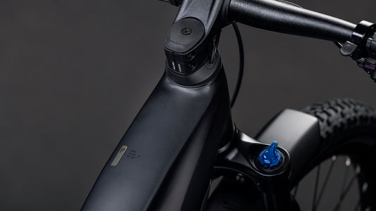 Nahaufnahme des mattschwarzen CUBE Reaction Hybrid Pro 800 FE blackline 2026 E-Bike-Rahmens und -Lenkers mit blauer Federgabelverstellung, angetrieben durch den Bosch CX-Motor für verbesserte Leistung, vor dunklem Hintergrund.