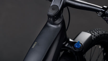 Nahaufnahme des mattschwarzen CUBE Reaction Hybrid Pro 800 FE blackline 2026 E-Bike-Rahmens und -Lenkers mit blauer Federgabelverstellung, angetrieben durch den Bosch CX-Motor für verbesserte Leistung, vor dunklem Hintergrund.