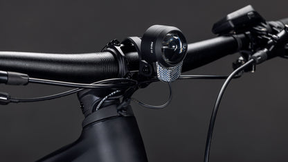 Nahaufnahme des CUBE Reaction Hybrid Pro 800 FE blackline 2026 Lenkers mit Kabeln, montiertem Frontlicht und reflektierendem Panel vor einem dunklen Hintergrund - mit fortschrittlicher Technik wie dem Bosch CX Motor und der Shimano XT Schaltung.