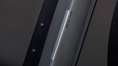 Nahaufnahme eines metallischen Etiketts mit der Gravur REACTION auf dem CUBE Reaction Hybrid Pro 800 FE blackline Easy Entry 2026, das mit zwei Schrauben befestigt ist. Der Bosch CX Motor im Hintergrund ist leicht verschwommen.