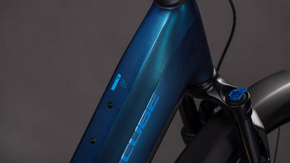 Nahaufnahme des Cube Reaction Hybrid Pro 800 FE nebular'n'dazzle Easy Entry 2026 von CUBE, die den blauen Rahmen mit Logo, Oberrohr, Vorderradgabel und Batterieanzeige hervorhebt. Das E-Bike hebt sich vor einem unscharfen grauen Hintergrund ab.