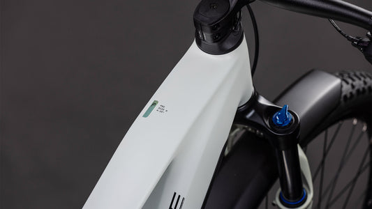 Nahaufnahme des Cube Reaction Hybrid Pro 800 FE desertstone'n'driedherbs 2026 von CUBE mit seinem modernen weißen Rahmen, der Digitalanzeige am Oberrohr, dem sichtbaren Lenker, der Federgabel und den strukturierten Reifen vor einem dunklen Hintergrund.