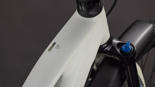 Nahaufnahme des CUBE Cube Reaction Hybrid Pro 800 FE desertstone'n'driedherbs Trapeze 2026 E-Bike-Rahmens in der Nähe des Lenkers, die eine kleine LED-Anzeige mit Akku- und Leistungsinformationen vor einem dunklen Hintergrund zeigt.