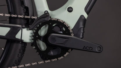 Nahaufnahme des CUBE Reaction Hybrid Pro 800 FE Trapeze 2026 in desertstone'n'driedherbs mit schwarzer ACID-Kurbelgarnitur, Kettenblatt und Kette. In den grün-schwarzen Rahmen sind ein Bosch CX Motor und eine Shimano XT 12-fach Schaltung integriert; der Hinterreifen ist teilweise zu sehen.