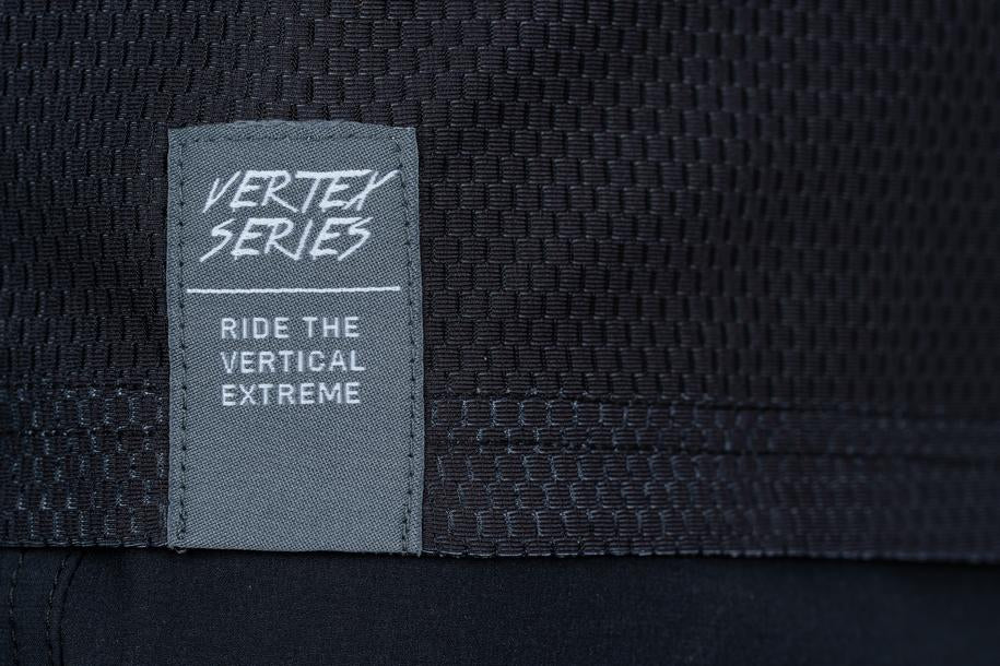 Nahaufnahme des Cube VERTEX Rundhalstrikots langarm schwarz, mit strukturiertem Stoff und einem grauen Etikett mit "VERTEX SERIES" und "RIDE THE VERTICAL EXTREME" in weißer Schrift; für die Kompatibilität mit Nackenbügeln konzipiert.