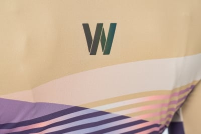Nahaufnahme des CUBE TEAMLINE WS Trikot kurzarm violet'n'sand von Cube, mit stilisiertem W-Logo in Grün und Dunkelgrau mit geschwungenen lila, rosa und weißen Linien - ideales Kurzarmtrikot-Design für sportliche Radfahrerinnen.