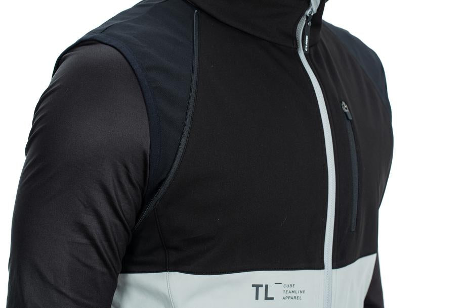 Nahaufnahme einer Person, die die CUBE TEAMLINE Multifunktionsjacke black'n'grey trägt. Sie hat abnehmbare Ärmel, eine Brusttasche mit Reißverschluss, wind- und wasserabweisendes Material und das CUBE Logo auf der Vorderseite.