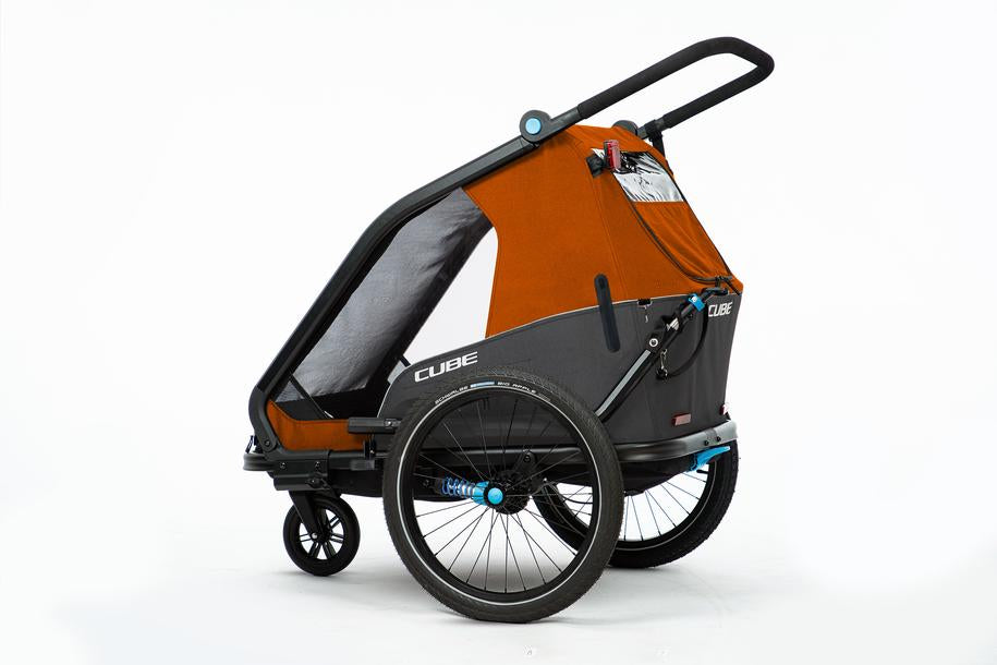 Der CUBE Kinder Fahrradanhänger Double CMPT X Actionteam von Cube ist ein moderner, orange-schwarzer, zweirädriger Kinderfahrradanhänger mit großem Lenker und transparenter, insektengeschützter Seitenabdeckung, abgebildet auf weißem Hintergrund.