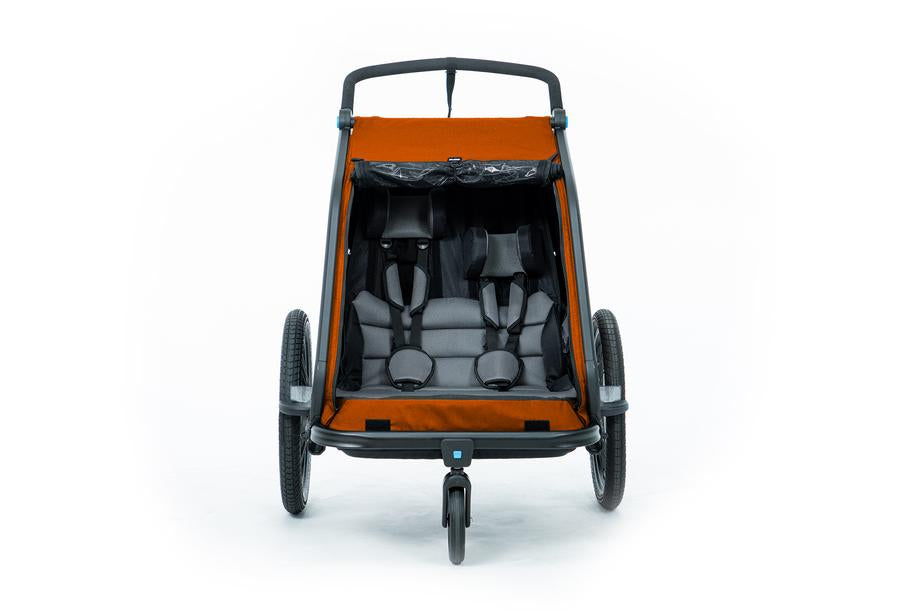 Vorderansicht des Cube CUBE Kinder Fahrradanhänger Double CMPT X Actionteam, eines orangefarbenen Doppelfahrradanhängers und Kinderwagens mit zwei Sitzen, Gurten, drei Rädern und Insektenschutz, entwickelt für Kinder. Abgebildet leer vor weißem Hintergrund.
