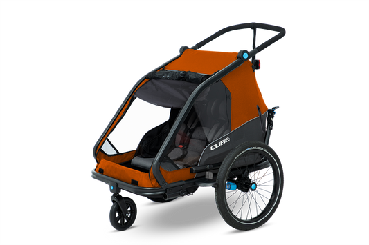 Der Cube CUBE Kinder Fahrradanhänger Double CMPT X Actionteam ist ein orange-schwarzer Kinderfahrradanhänger mit einem Insektenschutzgitter, zwei Sitzen, drei Rädern und einer hinteren Lenkstange, abgebildet auf einem schlichten weißen Hintergrund.