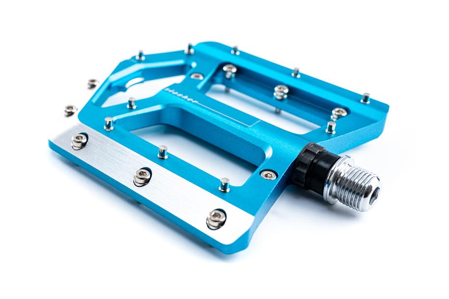 Eine Nahaufnahme des flachen Cube Pedale SLASHER Fahrradpedals mit großer Standfläche, metallenen und einstellbaren Pins und einer silbernen Spindel, isoliert auf weißem Hintergrund.