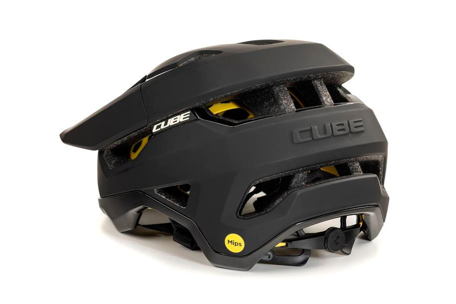 Ein schwarzer Cube Helm TROOPER / MTB Enduro Helm mit Visier, gelbem MIPS Sicherheitsaufkleber und Belüftungslöchern ist auf weißem Hintergrund abgebildet.