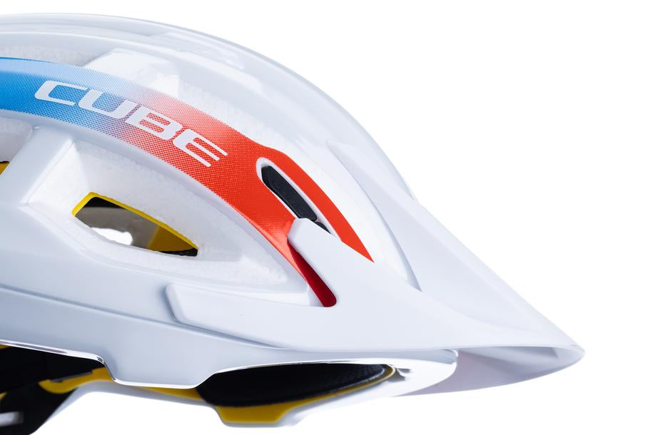 Nahaufnahme des Cube CUBE Helm OFFPATH Teamline weiß / MTB Race Helm, mit roten, blauen und weißen Streifen, Belüftungslöchern, einem Visier, Double-In-Mould Konstruktion und Cube Branding auf weißem Hintergrund.