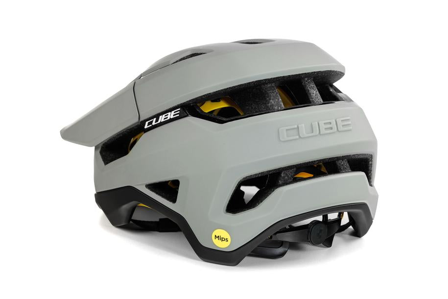 Der CUBE Helm TROOPER von Cube ist ein mattgrauer Enduro-Helm mit schwarzen und gelben Akzenten, Belüftungskanälen, einem verstellbaren hinteren Riemen und einem kleinen gelben Aufkleber, der auf die MIPS-Technologie für mehr Sicherheit hinweist.
