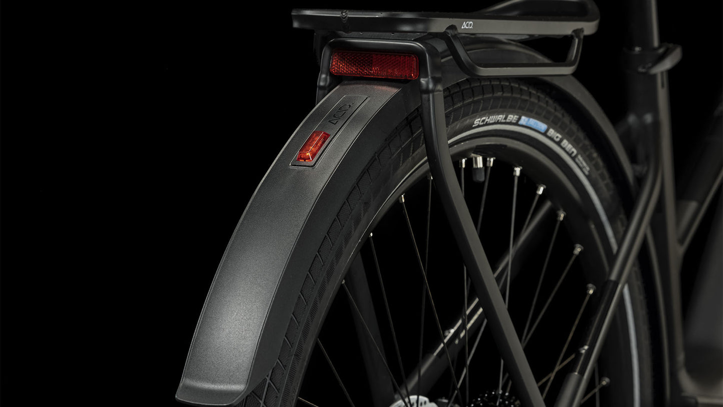 Nahaufnahme des Hinterrads eines CUBE Touring Hybrid Pro 625 black'n'metal Trapeze 2024, wobei das Schutzblech, der Reifen, die Speichen, der Gepäckträger und der rote Reflektor vor einem schwarzen Hintergrund hervorgehoben werden.
